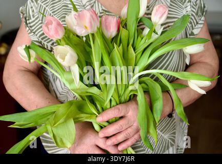Femme méconnaissable en robe de sequins argentés tenant un bouquet de tulipes roses, Banque D'Images