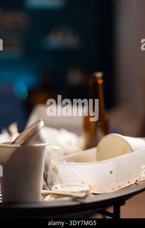 Videz les canettes de nourriture sales et les bouteilles de bière laissées sur une table non organisée recouverte de restes de déchets et de poubelles salissantes. Poubelles malsaines puantes dans un espace de salon chaotique désordonné. Gros plan. Banque D'Images