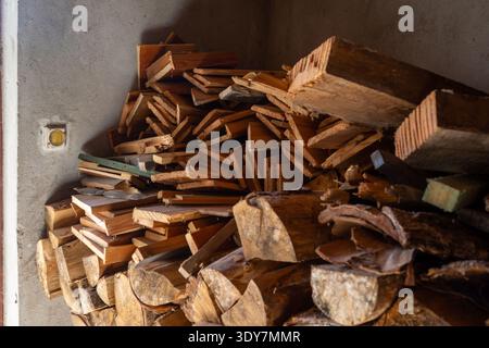 Brouette pour le travail de cour bûches de bois empilées dans une salle de stockage sombre, tailles assorties et textures d'écorce, naturelles Banque D'Images