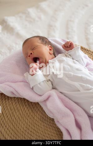 Bébé nouveau-né Yawning dans le panier en osier sur couverture rose souple Banque D'Images