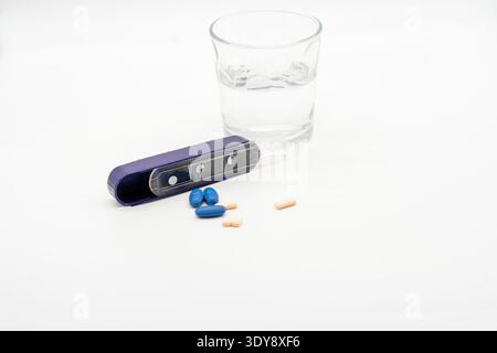 Verre d'eau avec organisateur de pilule et capsules bleues et beiges dispersées sur fond blanc Banque D'Images