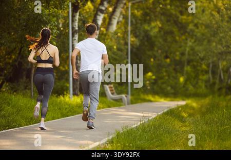 Vue arrière d'un jeune couple sportif qui court sur le sentier du parc et profite d'un jogging matinal en plein air. Banque D'Images
