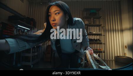 Jeune femme asiatique dans élégant Trench Coat se penche dans Collect Shopping Bags et packages. Femelle rassemble soigneusement ses achats. Vue prise depuis l'intérieur du coffre. Concept de Urban Lifestyle moment. Banque D'Images