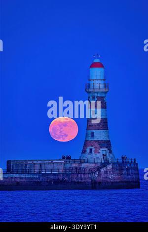 Une vue au crépuscule de la pleine lune de mars vers un ciel clair au-dessus de Roker Pier et phare à Sunderland, Tyne & Wear Banque D'Images