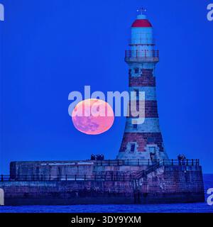 Une vue au crépuscule de la pleine lune de mars vers un ciel clair au-dessus de Roker Pier et phare à Sunderland, Tyne & Wear Banque D'Images