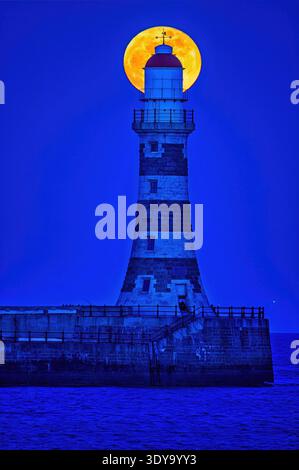 Une vue au crépuscule de la pleine lune de mars vers un ciel clair au-dessus de Roker Pier et phare à Sunderland, Tyne & Wear Banque D'Images