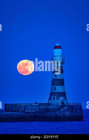 Une vue au crépuscule de la pleine lune de mars vers un ciel clair au-dessus de Roker Pier et phare à Sunderland, Tyne & Wear Banque D'Images