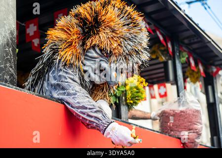 Bâle, Suisse - 25 mars 2026 : participant masqué au carnaval jetant des confettis d'un char de défilé lors de la célébration du Fasnacht de Bâle dans le HIS Banque D'Images