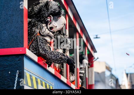 Bâle, Suisse - 25 mars 2026 : participant masqué sur un char de carnaval jetant des bonbons à la foule pendant le traditionnel défilé du Fasnacht de Bâle Banque D'Images
