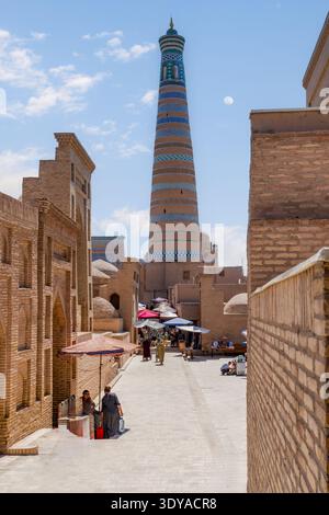 Khiva, province de Khorezm, Ouzbékistan - 31 mai 2025 : Rue étroite de briques menant au minaret Islam Khoja sous Un ciel bleu avec lune à Itchan Kala Banque D'Images