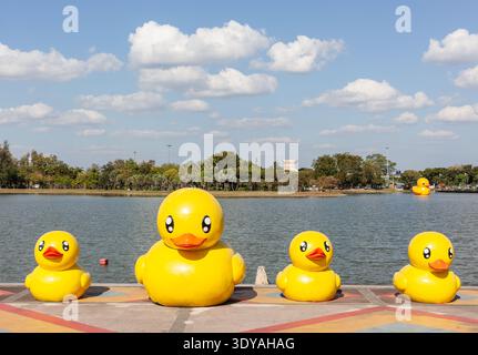 Canards géants en caoutchouc jaune flottant sur un lac dans un parc à Udon Thani. Grands canards gonflables sur l'eau avec des arbres et le ciel en arrière-plan. Banque D'Images