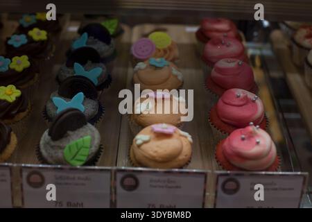 Rangées de cupcakes décorés avec divers glaçages, y compris du chocolat, des biscuits et de la crème, de la pêche et de la fraise exposés derrière un verre dans un café. Topp Banque D'Images