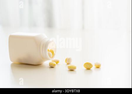 Pilules de médecine renversant la bouteille de pilule sur fond de table blanc. Banque D'Images