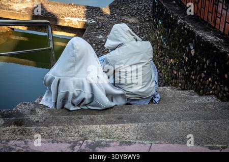 Deux amis en sweats à capuche assis près l'un de l'autre sur des marches en béton Banque D'Images