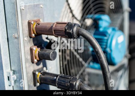 Fiche électrique robuste avec collier de verrouillage fileté connecté à l'armoire de commande métallique, câble noir courbé vers les machines, puissance industrielle Banque D'Images