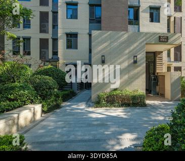 Une photo de paysage d'une entrée d'immeuble moderne avec un sol pavé de pierre et des haies bien entretenues dans un jardin communautaire serein. Banque D'Images