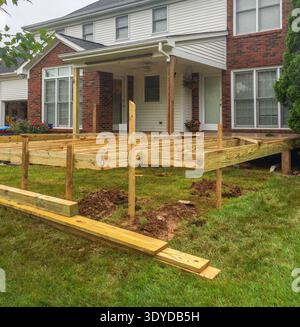 Terrasse en bois en construction à côté de la maison en briques. Les poutres de support s'élèvent de la cour herbeuse. Les planches de terrasse forment une fondation solide. Le porche de la maison offre cov Banque D'Images