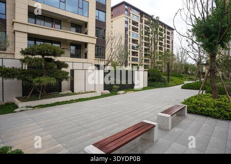 Un jardin propre et moderne doté d''un banc en bois et d''un mur en pierre, entouré d''arbres. L'image véhicule la simplicité, les loisirs de la communauté, Banque D'Images