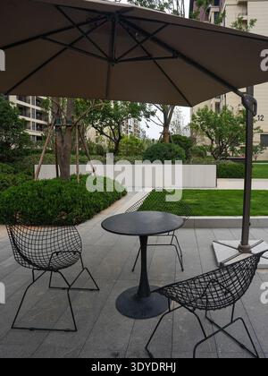 Un gros plan d'une salle à manger moderne en plein air sur un patio en pierre, entouré d'une verdure vibrante et d'une lumière douce du soleil. L'image véhicule des leis d'extérieur raffinés Banque D'Images
