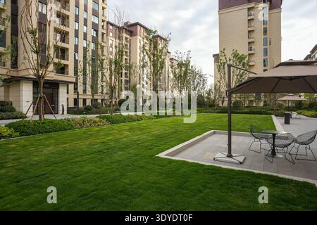 Un parc résidentiel calme et ensoleillé avec une pelouse verte et un patio extérieur assis contre des immeubles d'appartements modernes. L'image transmet relaxati Banque D'Images