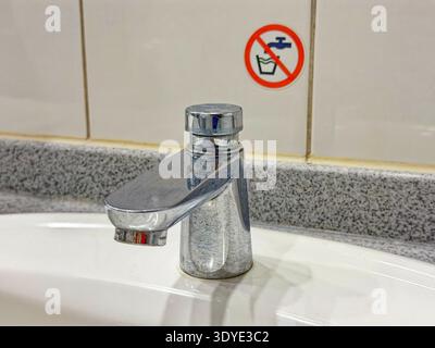 Un robinet en métal brillant est monté sur un évier blanc avec un comptoir en granit et un signe d'absence d'eau potable sur le mur carrelé derrière lui. Banque D'Images