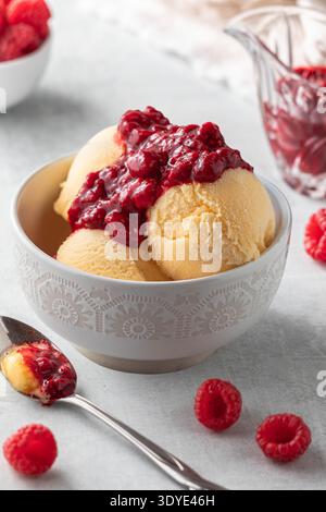 Un bol de sorbet de mangue sucré et crémeux garni de coulis de framboises. Banque D'Images