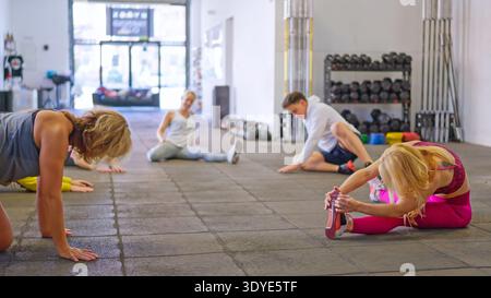 Groupe de personnes s'étirant sur le sol pendant l'entraînement de fitness Banque D'Images