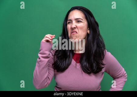 Femme grimacant, se pinçant le nez, et montrant le dégoût d'odeur désagréable ou mauvaise odeur sur fond vert Banque D'Images