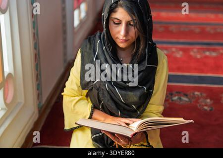 Une femme musulmane portant un foulard lit le Coran dans une mosquée. Banque D'Images