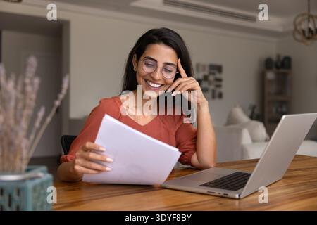 Femme tenant une pile de documents, lisant des informations avec une expression satisfaite Banque D'Images