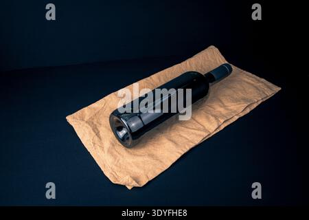 Bouteille de vin non étiquetée couchée sur une serviette en tissu au-dessus d'une surface sombre, photographiée avec une lumière sombre comme une nature morte minimaliste sur le service, la préparation Banque D'Images