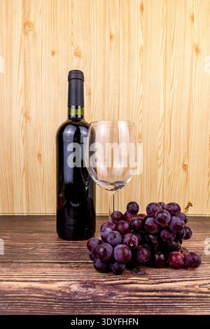 Bouteille de vin rouge avec un verre vide et raisins rouges sur une table en bois rustique, nature morte chaude pour le vignoble, la récolte, l'hospitalité, le restaurant et bevera Banque D'Images