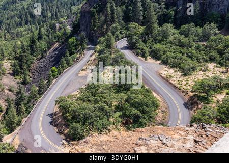 La route sinueuse traverse une forêt verdoyante. Les lignes jaunes guident les conducteurs le long de la descente abrupte. Châssis rocheux à flanc de falaise chemin sinueux en dessous. Lumière solaire filte Banque D'Images