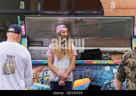 Une femme portant un chapeau de camionneur rose et une chemise teintée sourit tout en assistant à son vibrant camion de vendeur couvert d'art à Panama City, en Floride. Elle est PA Banque D'Images