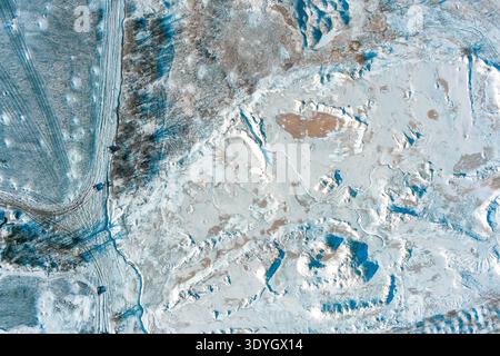 Cette fosse industrielle en argile recouverte de neige présente des lignes d'excavation profondes et des traces de pneus. Un paysage gelé d'extraction de ressources capture la dure réalité des opérations minières hivernales et des textures. Banque D'Images