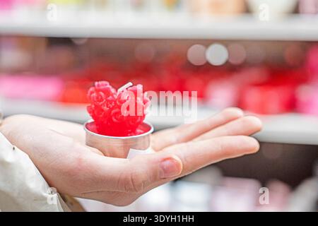 Un enfant tient une petite bougie rouge en forme de cœur dans sa paume. Banque D'Images