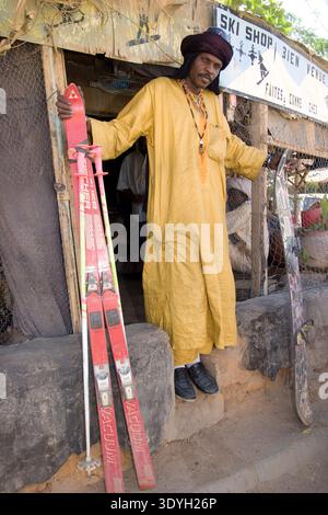 Touareg Man en dehors d'un magasin de ski de nouveauté offrant du ski sur les dunes de sable dans le désert du Sahara près d'Agadez, Niger, Afrique de l'Ouest. Banque D'Images