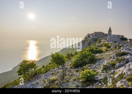 Petit village de pêcheurs (Lubenice) construit sur les rochers au-dessus de la mer avec une vue sur la mer par une journée ensoleillée au coucher du soleil sur l'île de Cres, Croatie Banque D'Images