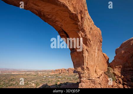 Vue panoramique sur North Window Arch dans le parc national d'Arches, Utah, encadrant le vaste paysage désertique et les formations rocheuses rouges sous un ciel bleu clair. Banque D'Images