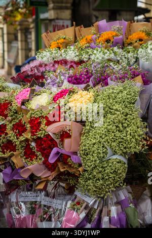 Exposition vibrante de bouquets de fleurs mélangées dans un étal de marché en plein air avec roses rouges, tournesols jaunes, roses pastel et délicat souffle de bébé Banque D'Images