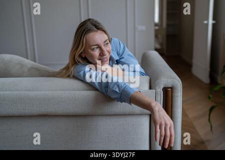 Heureuse femme mature heureuse se relaxant au canapé souriant insouciant profitant du temps conscient seul à la maison. Banque D'Images