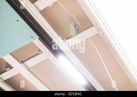 Vue rapprochée d'une installation de plafond suspendu avec éclairage LED intégré dans un système de rail noir dans un cadre intérieur moderne. Banque D'Images