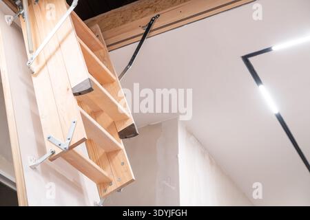 Échelle de grenier en bois prolongée vers le bas avec éclairage LED de plafond encastré moderne dans un intérieur de pièce simple. Banque D'Images