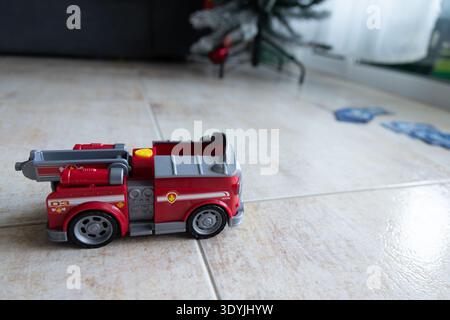 Le camion de pompiers rouge repose sur un sol carrelé. Les roues grises et les compartiments détaillés ajoutent du réalisme. Des accents jaune vif contrastent la peinture rouge vif. Arrière-plan Banque D'Images