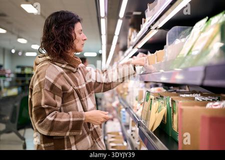 Femme magasinant en choisissant des produits alimentaires dans une allée de supermarché Banque D'Images