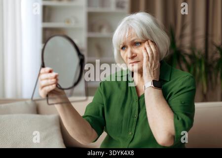 Femme senior regardant inquiet tout en vérifiant la peau dans le miroir Banque D'Images