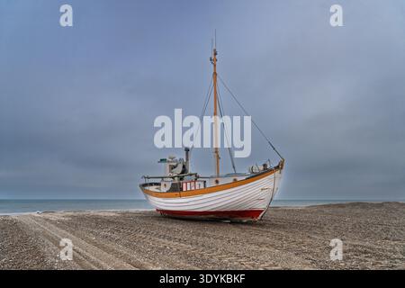 Deux bateaux de pêche en bois échoués reposent sur un rivage de galets sous un ciel couvert, véhiculant une atmosphère côtière tranquille, des textures altérées et la nautica Banque D'Images