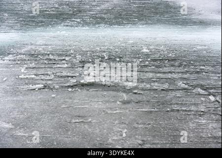 Gros plan de glace de lac gelée rugueuse avec des fragments de glace dispersés et des textures en couches, formant un fond hivernal abstrait froid avec gris et bleuté Banque D'Images