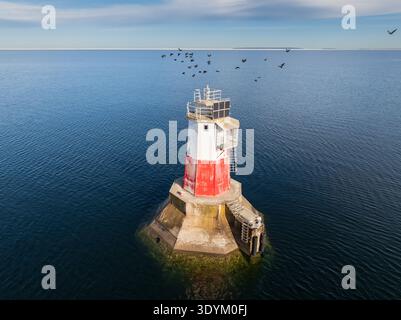 Vue aérienne de haut en bas d'un phare isolé rouge et blanc en mer sur un caisson en béton, avec panneaux solaires et une plate-forme d'amarrage, avec un flo Banque D'Images
