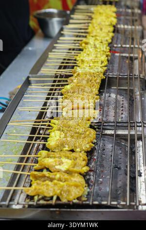 Satay de porc thaïlandais traditionnel sur un marché local. Brochettes de viande grésillantes avec épices pour guides de voyage et contenu promotionnel de l'industrie alimentaire. Banque D'Images